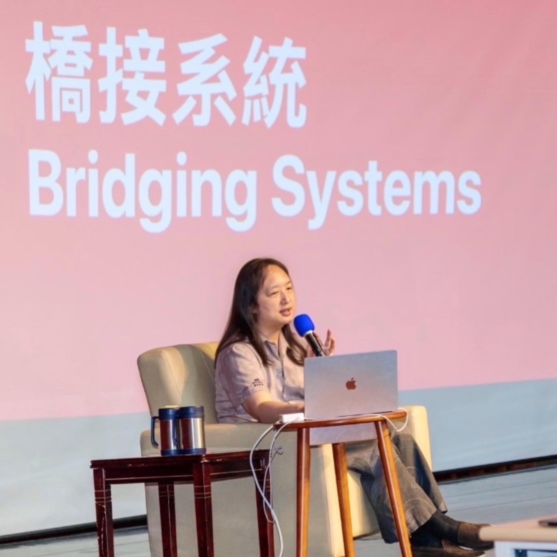 Audrey Tang on stage, sitting on a sofa, giving a speech with iA Presenter in the background